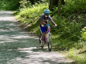 Sarah riding her bike and wearing a helmet on a path in the woods