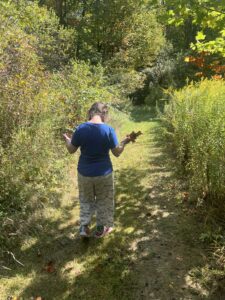 Sarah walking away from the camera with her head looking down and leaves in one hand 