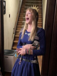 Amy in a blue dress with her hair down, laughing with her head thrown back and mouth wide 