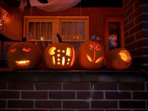 A photo taken at night with four glowing jack-o-laterns. The carvings depict a smiling face, a Pac-Man game, a flower, and a computer mouse. The computer mouse looks like an oval.