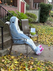 Jenny is sitting in a chair by her cement porch steps. You see her in profile, which just looks like a shark sitting while wearing large pink and white sneakers