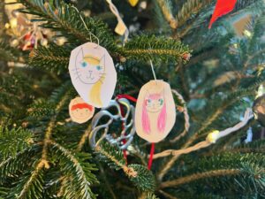 Close-up of pine tree branches with three paper ovals that have pictures of personified cats drawn on them to represent Amy through the years