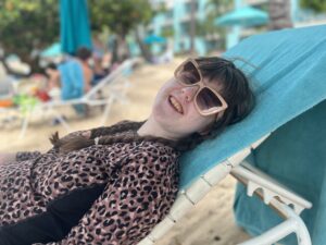 Sarah in a leopard print swim shirt reclining on a lounge chair on the beach and smiling