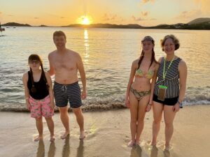 Sarah, Carl, Amy, and Jenny standing on a beach in swimsuits with the sunset behind them 