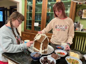 Sarah and Amy standing by the kitchen island decorating a gingerbread house