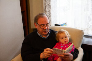 Jack reading a board book to Amy when she is maybe 2 years old. They are sitting in a beige chair together.