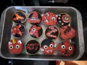 chocolate cupcakes in a tin with strawberry frosting and various candy eyes and sprinkles and fondant making them look like earnest creatures