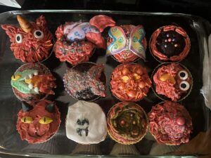 a tin of chocolate cupcakes with strawberry frosting and fondant making some look like butterflies or mermaid tails or cats or dragons