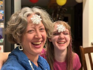 Jenny and Amy smiling while sitting next to each other and wearing white gift bows on their foreheads