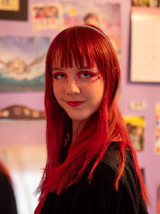 Close-up of Amy with vibrant red hair, black and red eye-makeup, and red gems on her cheeks.