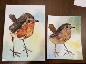 A painting of a bird (maybe a robin or wren) with a light blue background next to a watercolor of the same bird. The watercolor is Jenny's attempt at copying the original.