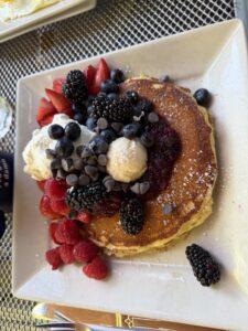 A pile of pancakes loaded with heaps of raspberries, strawberries, blackberries, whipped cream, and chocolate chips