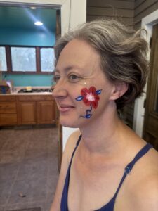 Side profile view of Jenny's face with a red heart shaped flower painted on her cheek by Amy. 