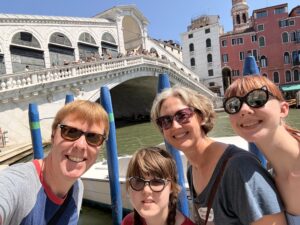 Carl, Sarah, Jenny, and Amy standing outside with the Rialto Bridge behind them. They are all wearing sunglasses and smiling. 