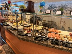 A curved display table with protective glass coverings beyond which are selections of donuts and cupcakes and bonbons galore.