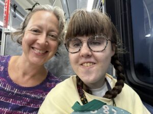A close-up photo of Jenny and Sarah as they ride the bus to Sarah's school. Jenny has a purple and white shirt and Sarah has a pale yellow sweatshirt. Sarah's hair is in two braids.